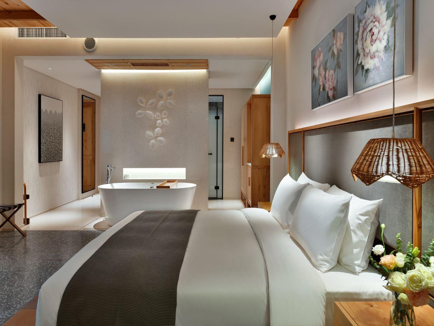 A modern hotel room with a large bed, a bathtub, and a wooden headboard.