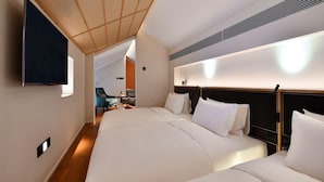 Una habitación de hotel con dos camas, un televisor montado en la pared y una pequeña zona de estar con sillas.