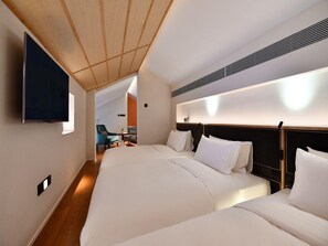 Una habitación de hotel con dos camas, un televisor montado en la pared y una pequeña zona de estar con sillas.