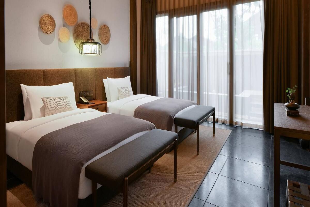 Ein Hotelzimmer mit zwei Betten, einem Schreibtisch und einem großen Fenster mit Vorhängen.