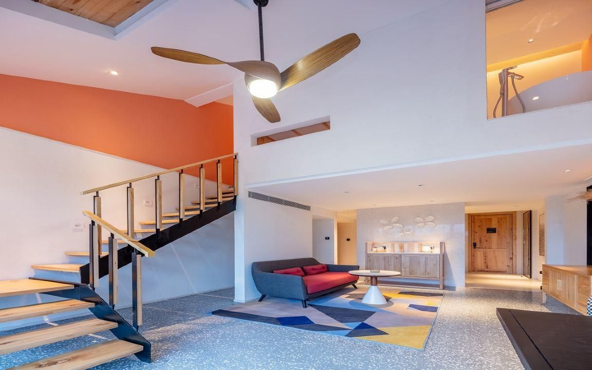 A modern interior with a staircase, a sofa, and a ceiling fan.