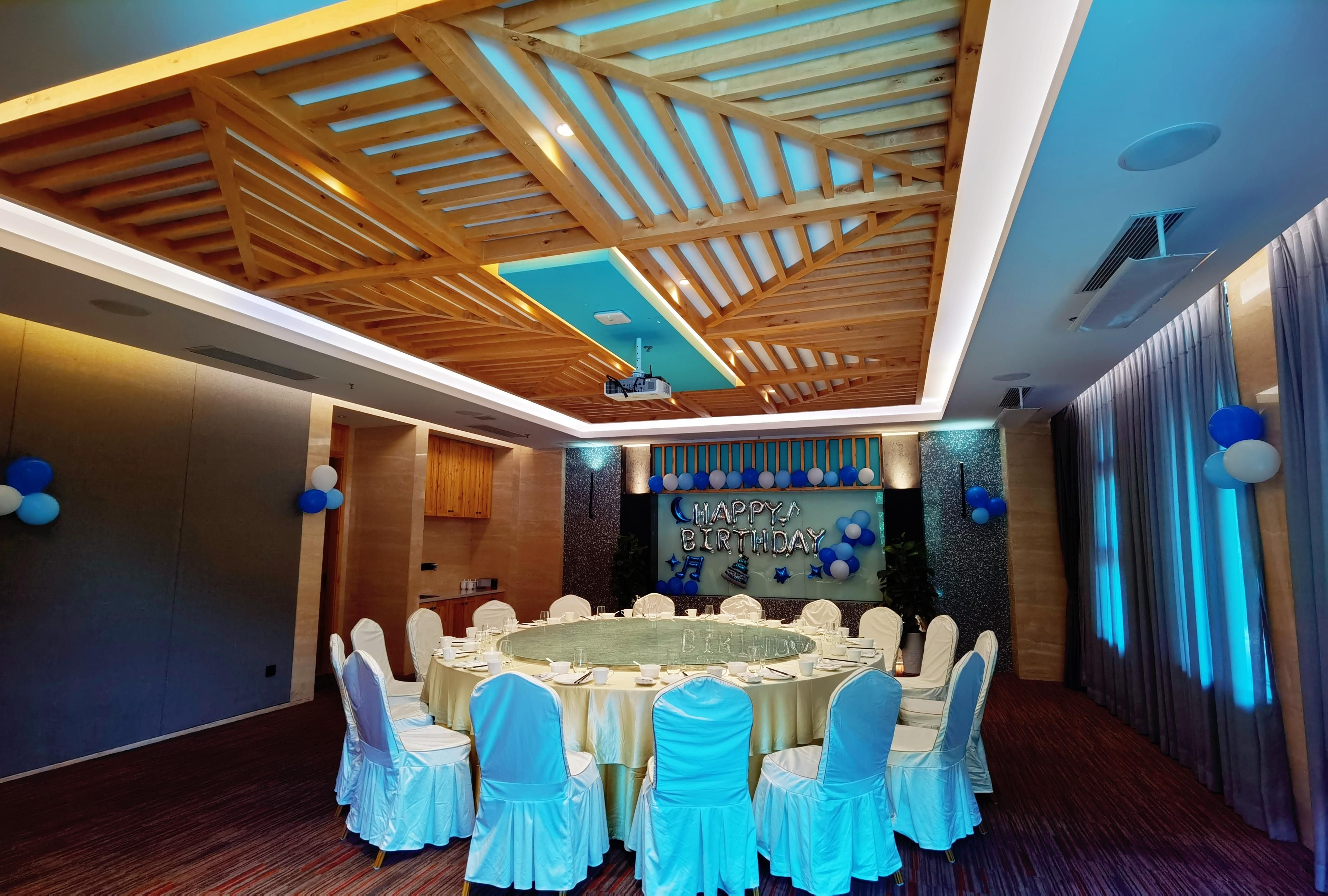A banquet hall with a high ceiling, wooden beams, and a central table surrounded by chairs.