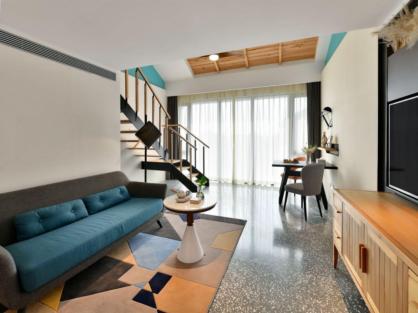 A modern living room with a sofa, a dining area, a staircase, and a TV.