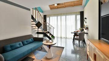 A modern living room with a sofa, a dining area, a staircase, and a TV.
