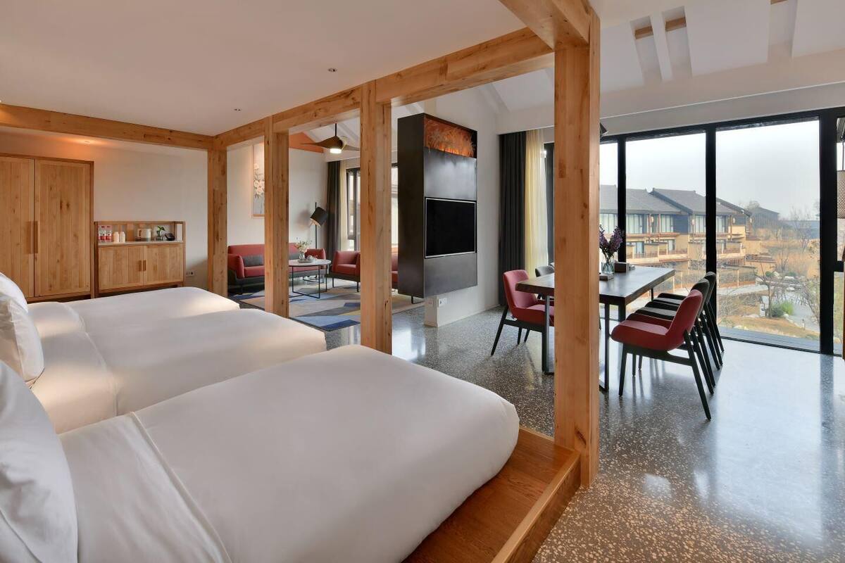 Ein modernes Hotelzimmer mit zwei Betten, einer Essecke und einem großen Fenster mit Blick auf die Umgebung.