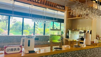 A bar area with a coffee machine, a tea station, and a view of a garden through large windows.