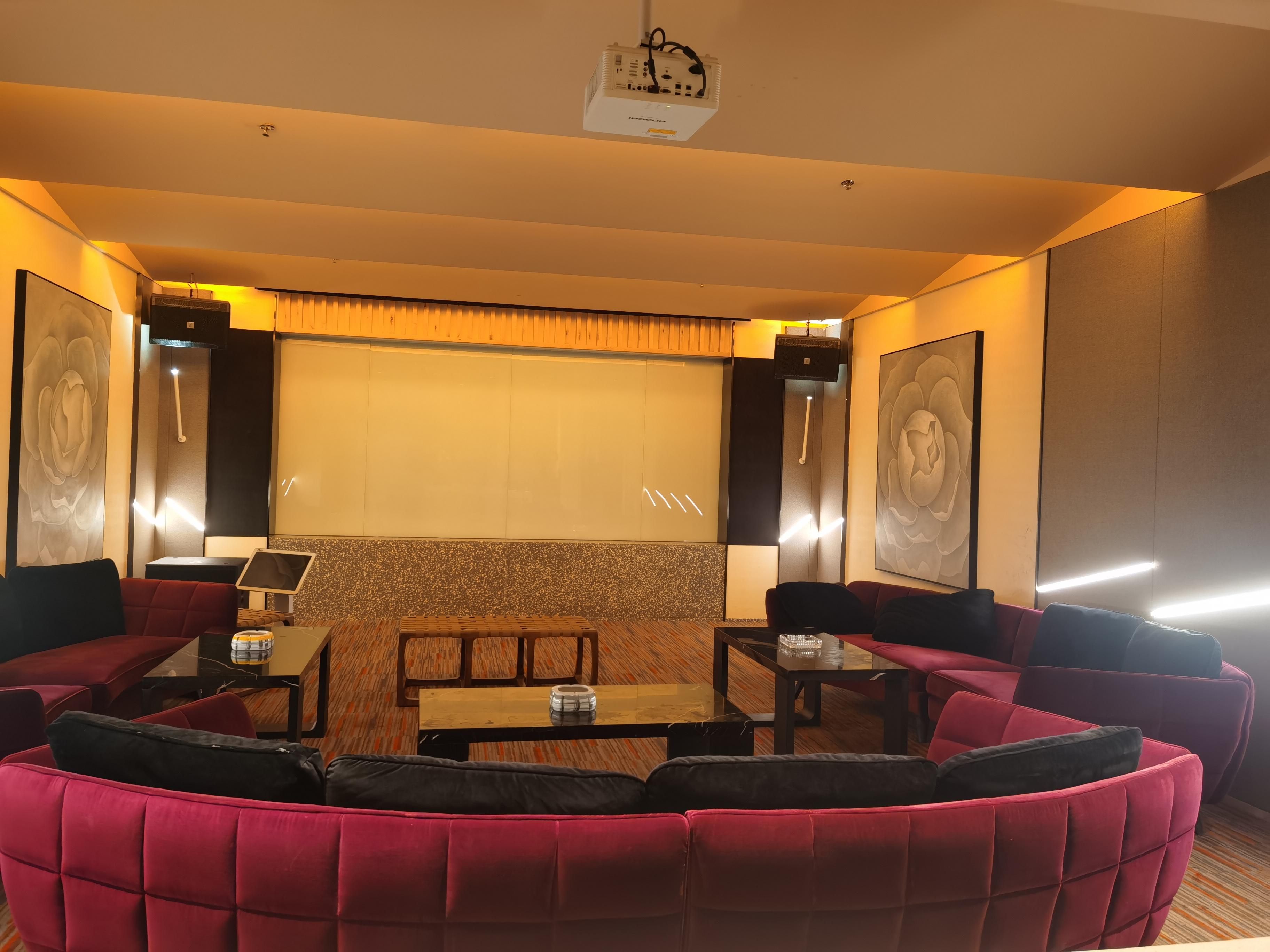 A modern lounge with a curved red sofa, a small wooden table, and a projector screen.