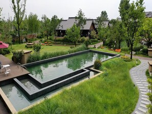 Ein rechteckiger Pool mit einem umgebenden Garten, einem Weg und traditionellen Gebäuden im Hintergrund.