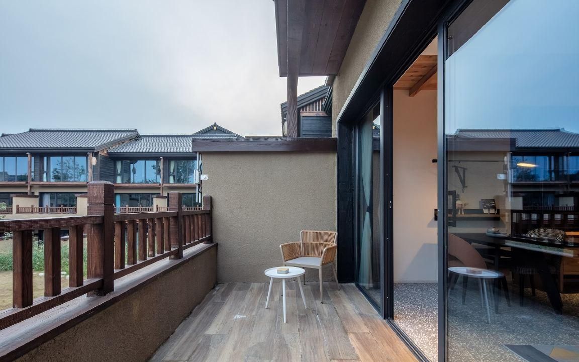 A balcony with a wooden railing, a small round table, and two wicker chairs.