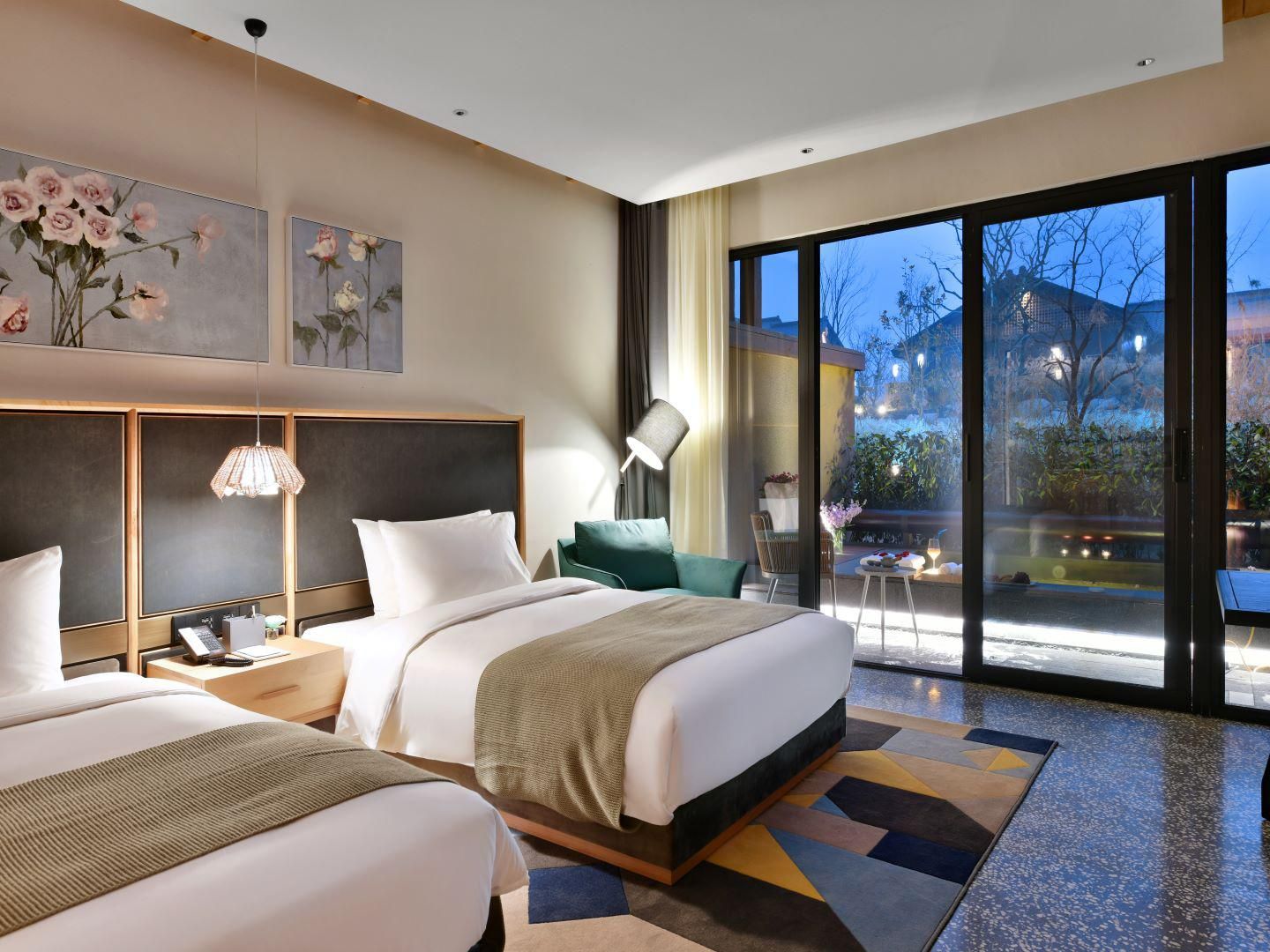 A modern hotel room with two beds, a large window, and artwork on the wall.
