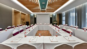 Un salón de conferencias con una larga mesa, sillas blancas y techo de madera.