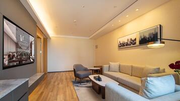 Uma sala de estar moderna com sofá, poltrona e mesa de centro. Há uma televisão de tela plana na parede e um quadro sobre o sofá.