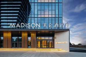 A modern hotel entrance with a glass facade, illuminated signage, and a clear sky.