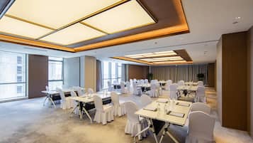 A conference room with multiple tables and chairs, large windows, and a high ceiling with recessed lighting.