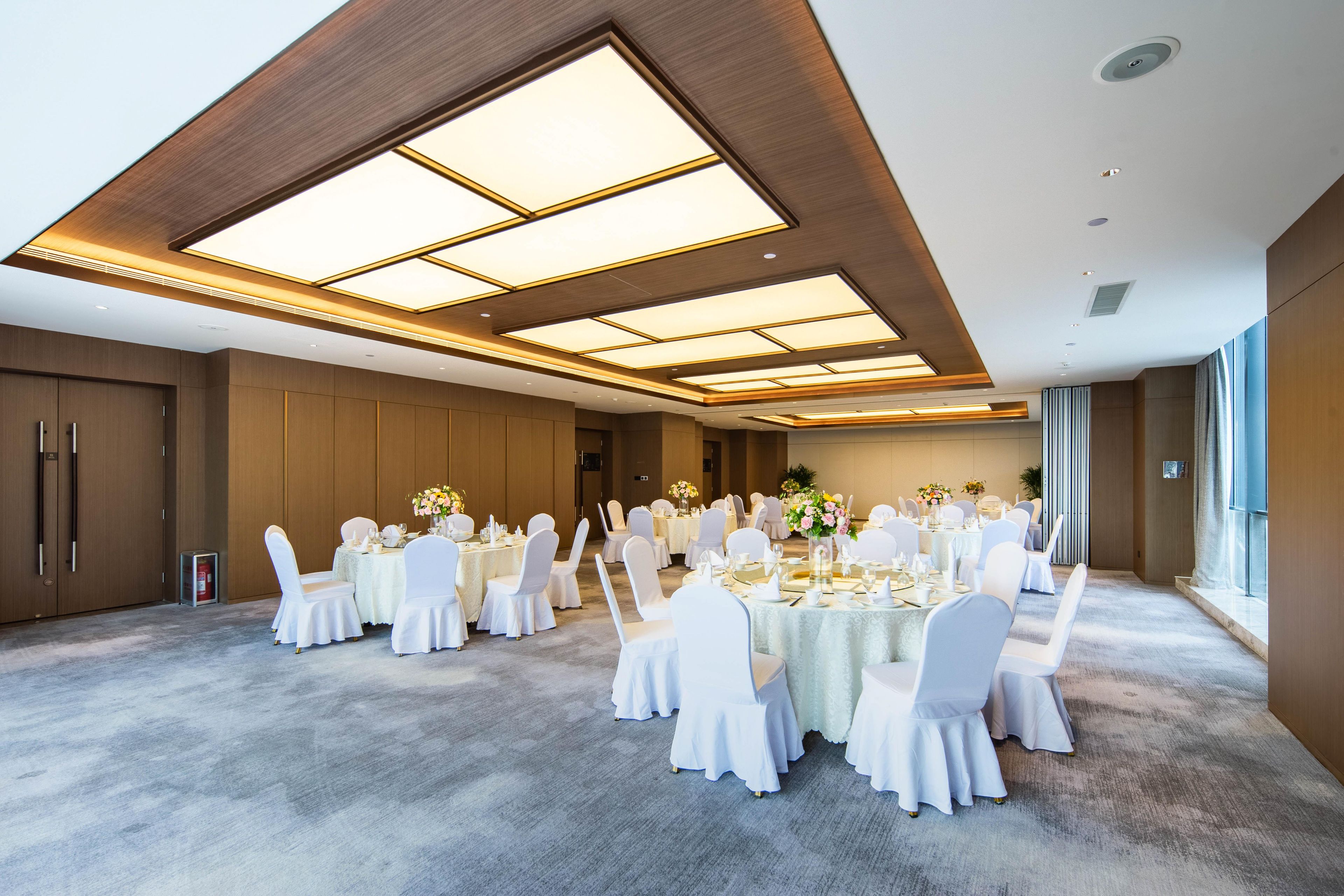 A large conference room with round tables, white chairs, and a high ceiling with skylights.