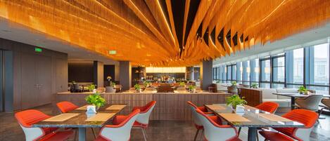 A modern dining area with a central bar, red and white chairs, and a ceiling with a unique light fixture.