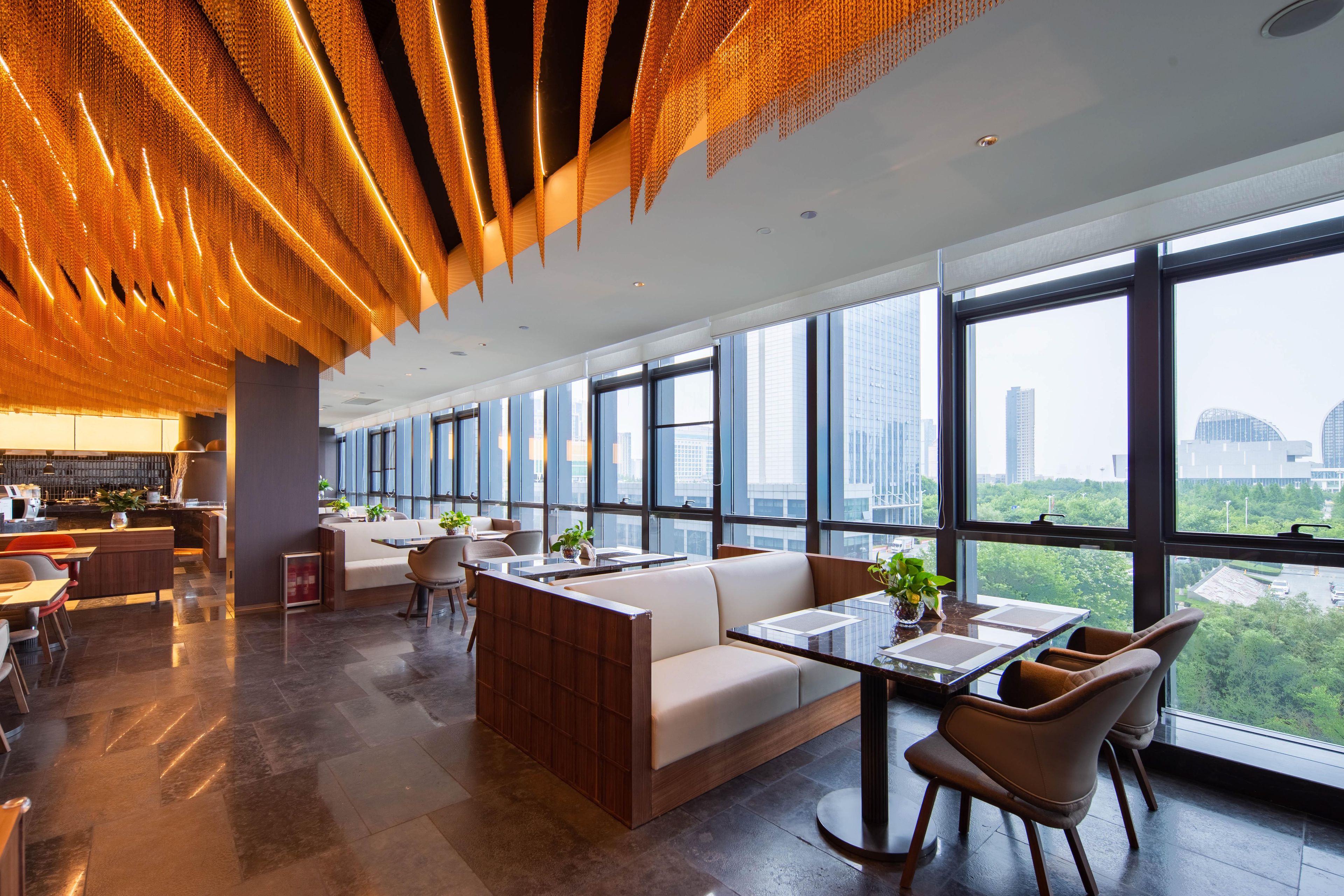 A modern interior with a long seating area, large windows, and a city view.