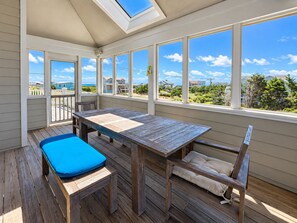 A covered patio with a wooden table and benches, large windows offering a view of a residential area. - C'EST FINI - Enjoy superb ocean views & great beach access from this 4,000 plus sqft. stunning home! (Southern Shores)