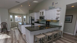 A kitchen with white cabinets, a granite countertop, and wooden stools. - C'EST FINI - Enjoy superb ocean views & great beach access from this 4,000 plus sqft. stunning home! (Southern Shores)