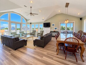 A spacious living room with a large dining table, comfortable seating, and a television. - C'EST FINI - Enjoy superb ocean views & great beach access from this 4,000 plus sqft. stunning home! (Southern Shores)