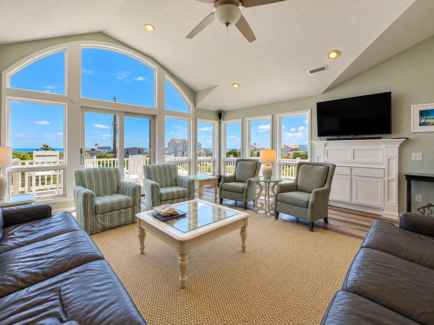 A spacious living room with large windows, a ceiling fan, and a flat-screen TV.