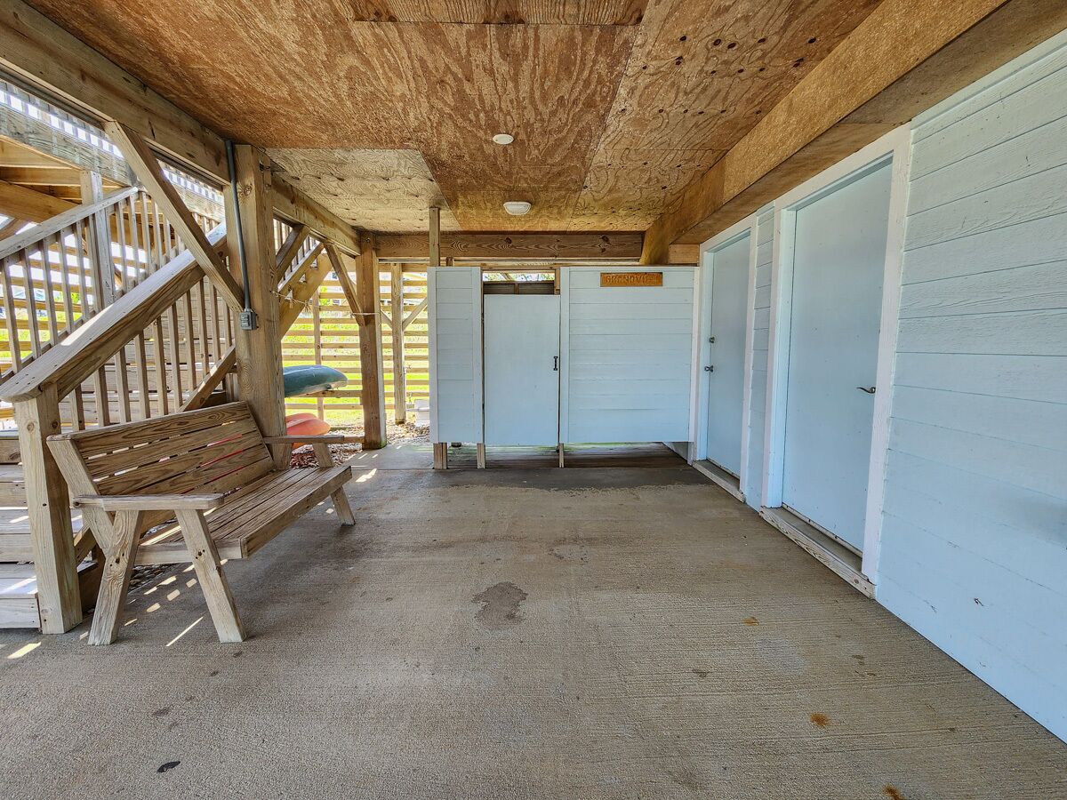 A covered outdoor area with a wooden bench, concrete floor, and a row of closed garage doors.