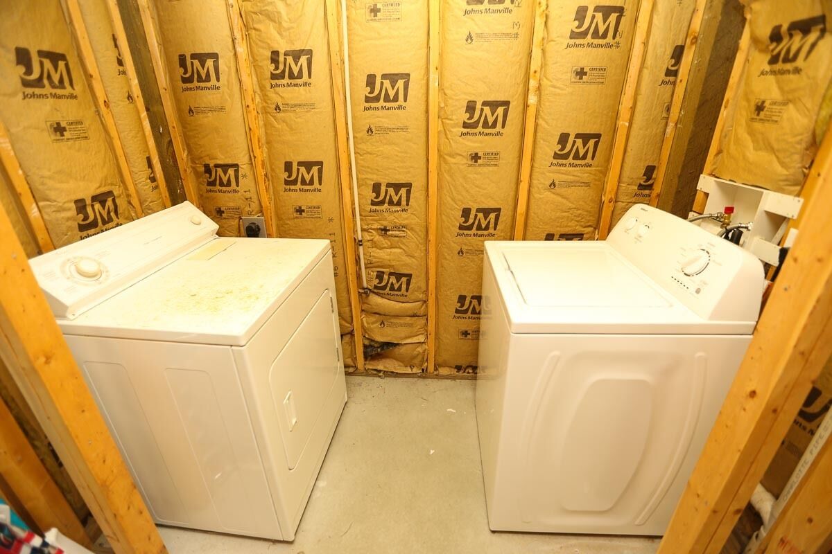 Une petite buanderie avec deux machines à laver blanches, des murs en bois et un matériau isolant portant la mention « Johns Manville ».