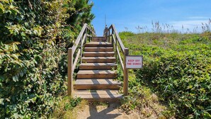 A wooden staircase leading up to a beach area with a 'KEEP OFF THE DUNES' sign.