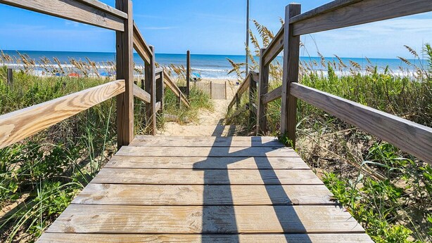 A wooden boardwalk leading to a beach with a clear view of the ocean.