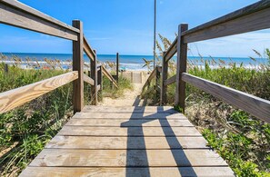 A wooden boardwalk leading to a beach with a clear view of the ocean.