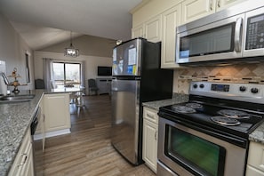A modern kitchen with stainless steel appliances, a granite countertop, and a view to the dining area. - Four Sandy Paws - Charming, home away from home, for you and you four-legged friend! (Duck)