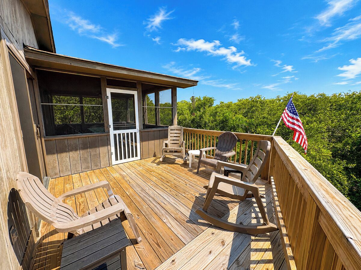 A wooden deck with outdoor furniture, a flag, and a view of trees.