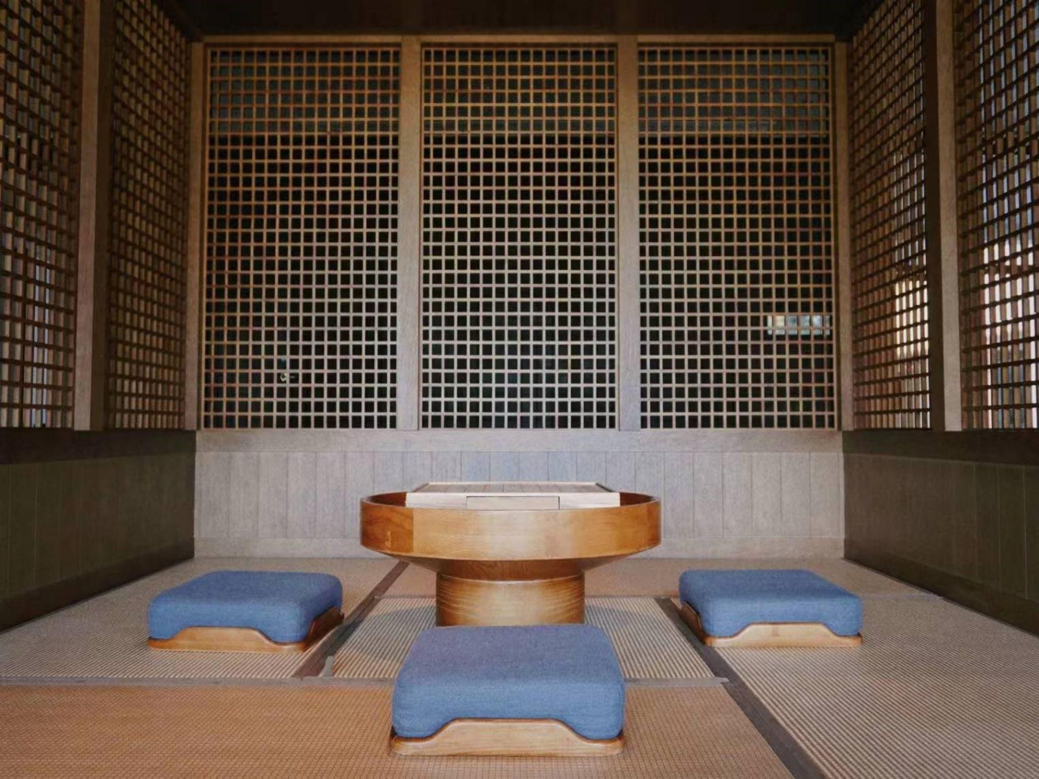 Una habitación tradicional japonesa con esteras de tatami, una mesa de madera central y cojines azules bajos.
