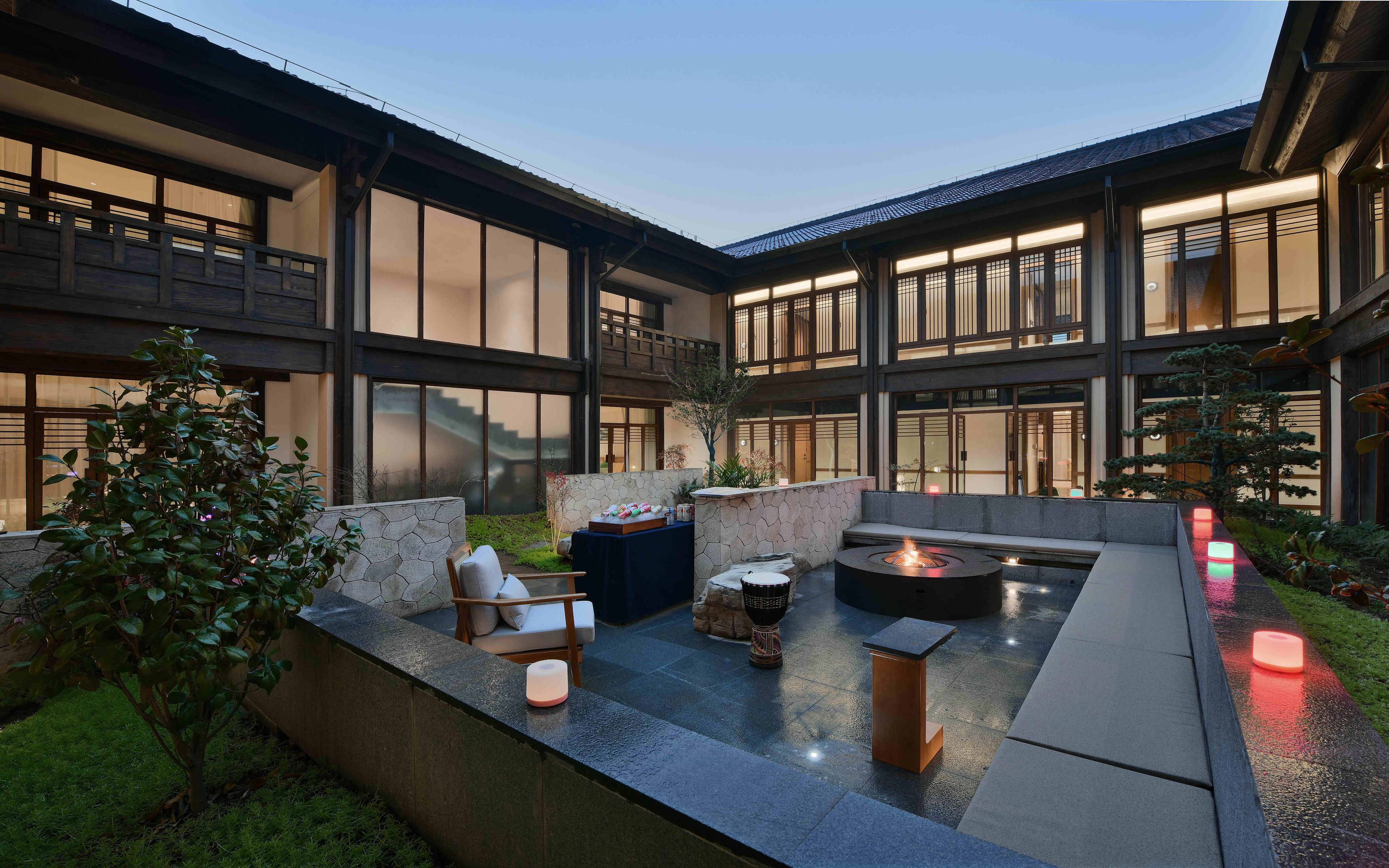 A modern outdoor patio with a fire pit, seating, and a stone wall.