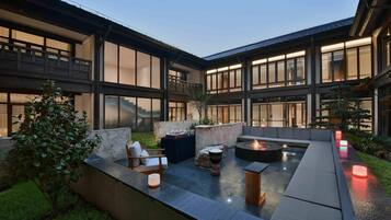 A modern outdoor patio with a fire pit, seating, and a stone wall.