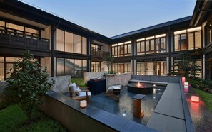 A modern outdoor patio with a fire pit, seating, and a stone wall.