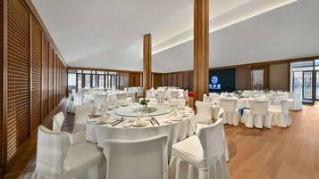 A banquet hall with round tables, white chairs, and a large screen displaying the hotel name.