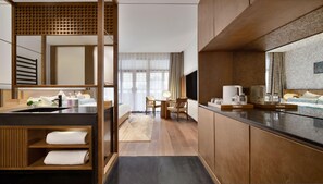 A hotel room with a wooden floor, a bed with white linens, a sitting area with a table and chairs, a kitchenette with a coffee maker, and a large window with curtains. - Blossom Hill Hotel Nanjing Lishui (Nanjing)