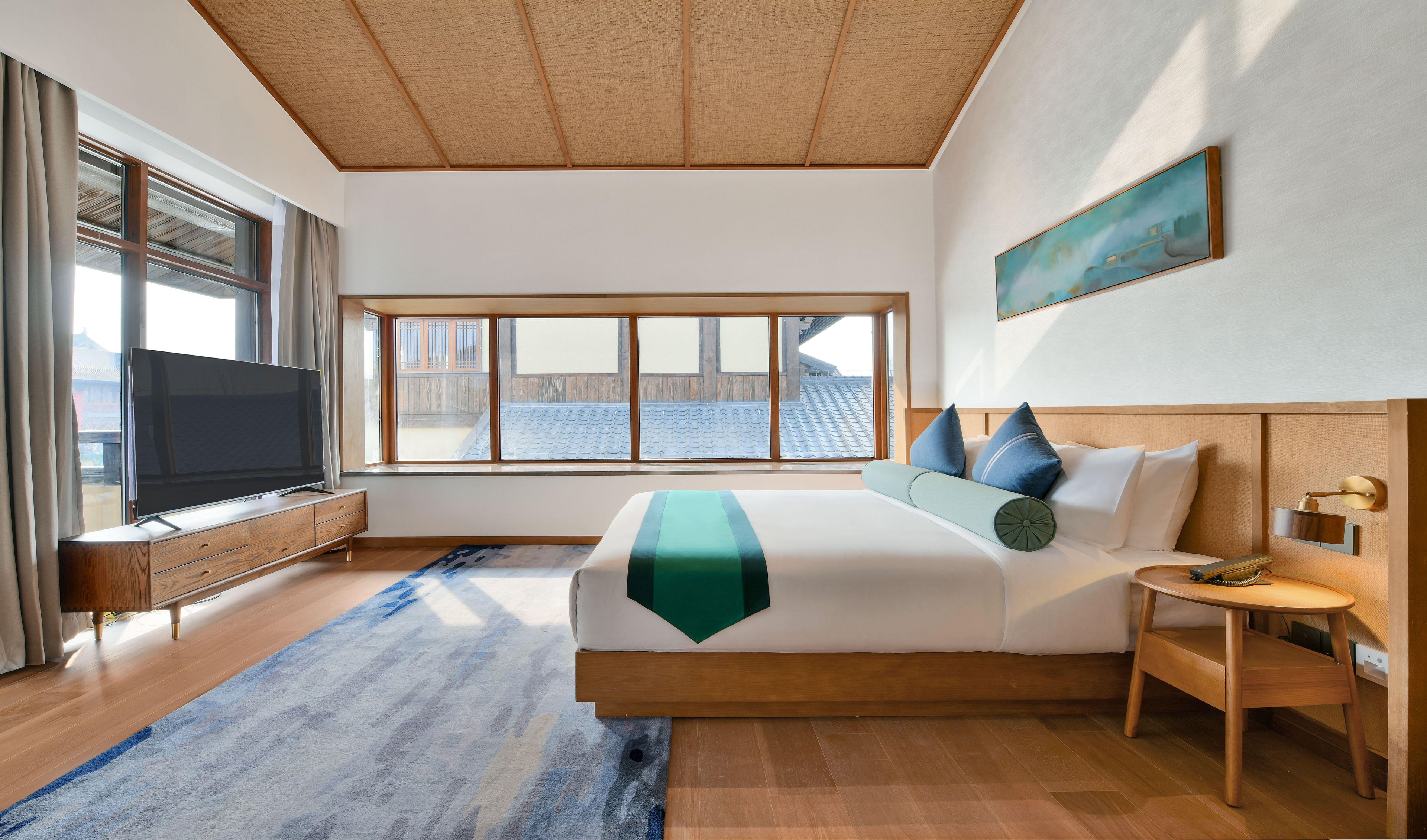 Een moderne hotelkamer met een groot bed, een televisie, een raam met uitzicht en een schilderij aan de muur.