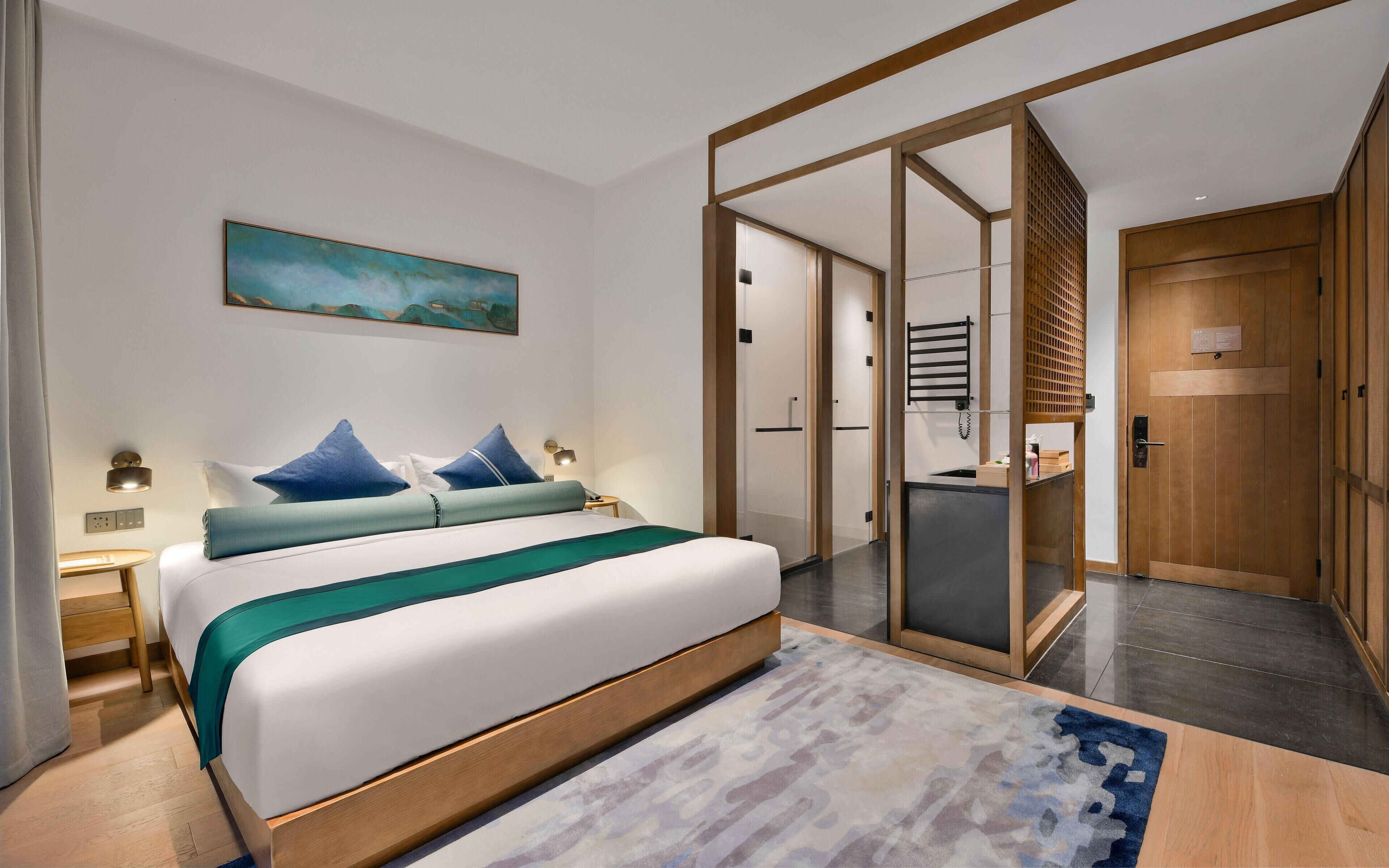 A modern hotel room with a large bed, a painting on the wall, and a sliding door leading to a bathroom.