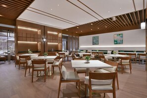 A spacious dining area with wooden tables and chairs, a modern ceiling design, and artwork on the walls. - Blossom Hill Hotel Nanjing Lishui (Nanjing)