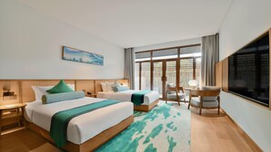 A hotel room with two beds, a sitting area with a table and chairs, a large window, and a painting on the wall. - Blossom Hill Hotel Nanjing Lishui (Nanjing)