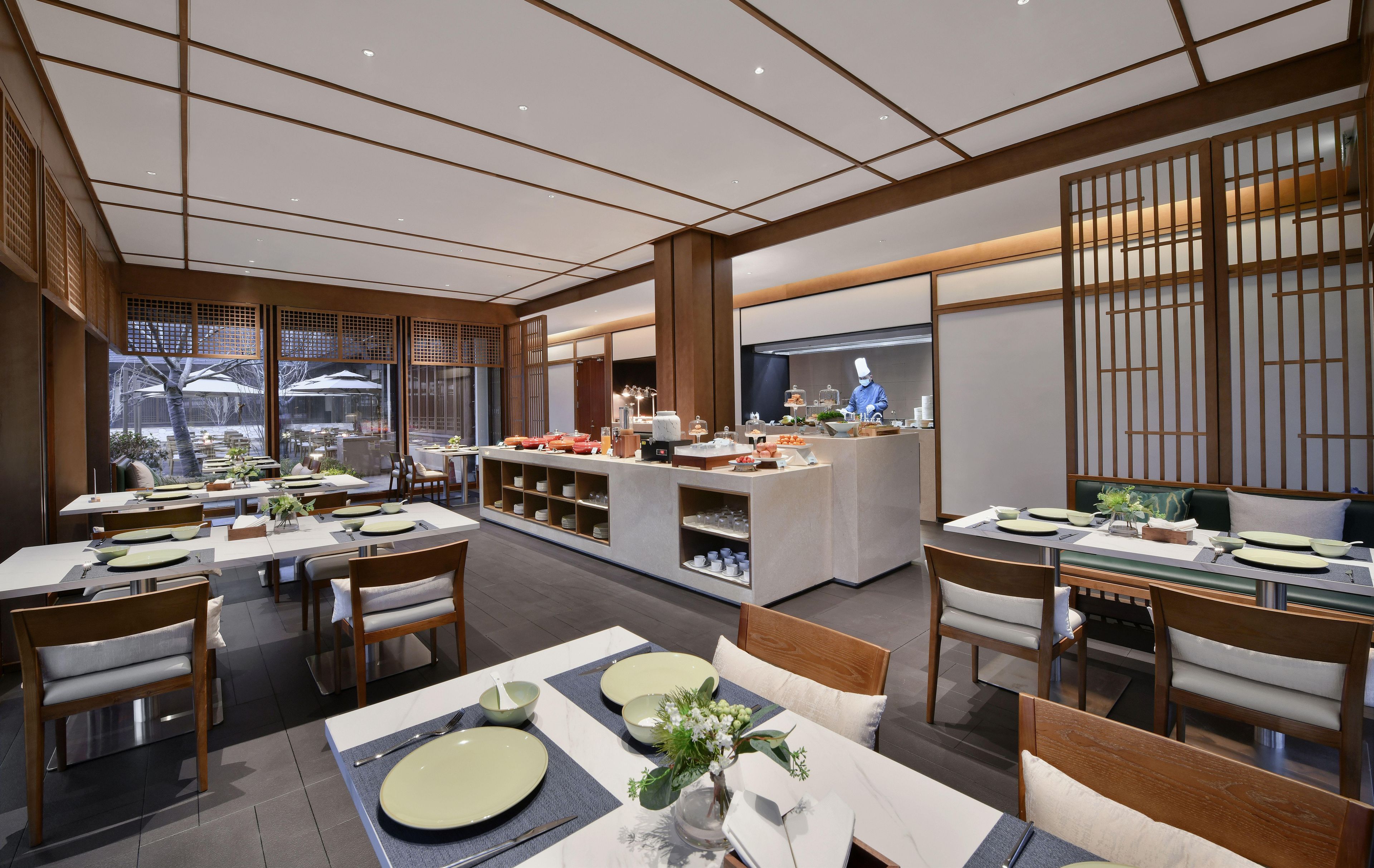 En modern restaurang med trämöbler, en central bardisk och utsikt över omgivningarna.