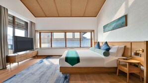 Habitación de hotel moderna con una cama grande, un televisor, una mesita de noche de madera y una ventana con vistas al tejado.