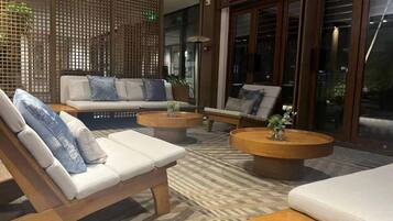 A modern lounge area with a sofa, armchairs, and a coffee table, featuring a patterned floor and wooden partitions.