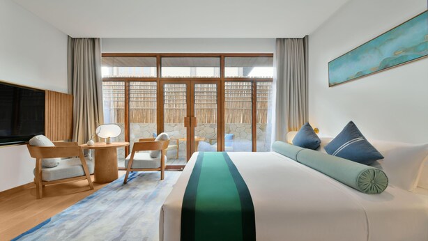 A hotel room with a large bed, a desk with a chair, a TV, and a balcony with a view. - Blossom Hill Hotel Nanjing Lishui (Nanjing)