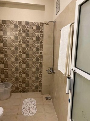 Shower area features a tiled wall with geometric and floral patterns, a towel rack, and a clear storage container.