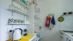 A compact kitchen with white cabinets, a yellow countertop, and various kitchenware on shelves.