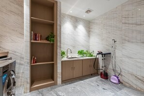 A bathroom with a built-in shelf, a sink with a modern faucet, a handheld vacuum cleaner, and a washing machine. - Crystal Orange Hotel Xinyi Center (Xuzhou)