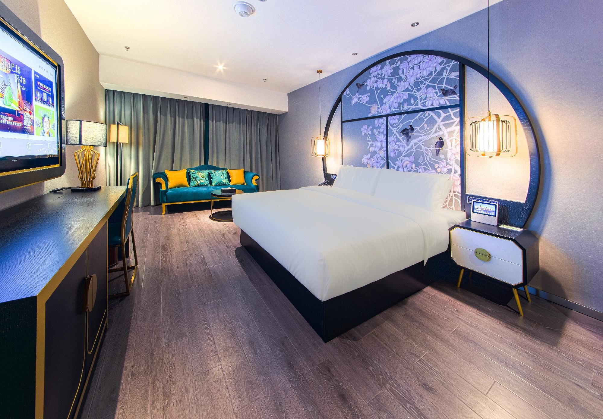 A hotel room with a large bed, a desk with a computer, a TV, and a wall with a decorative mural.